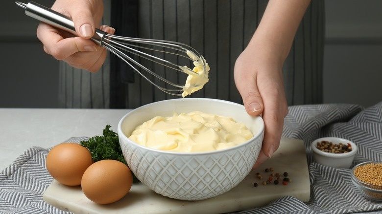 Visp med majonnäs över en skål, ägg och kryddor på köksbord